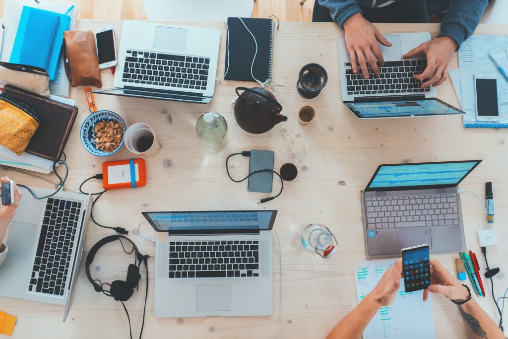 An overhead photo of people working on laptops and smartphones around a desk.